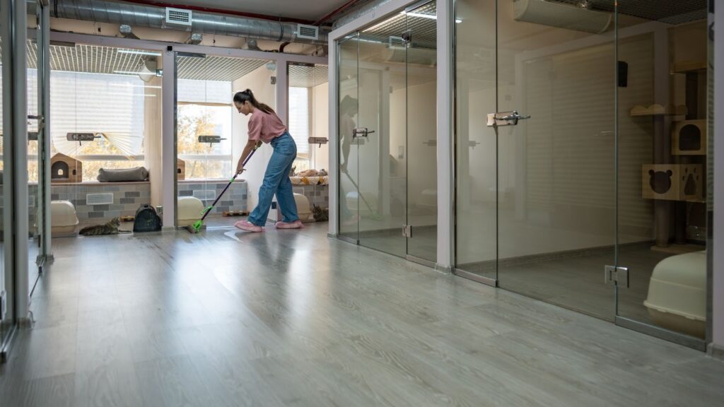 工作人員在現代化的寵物寄養中心走廊進行地板清潔，兩側為整潔的透明玻璃寵物房