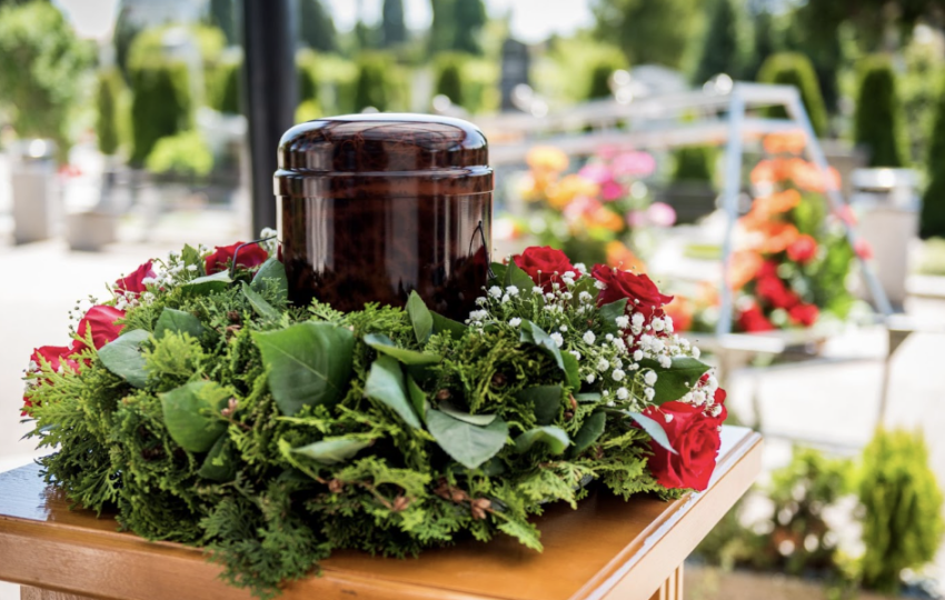 戶外墓園中擺放於木桌上的寵物骨灰罈，周圍以綠葉與紅玫瑰花圈環繞，氛圍莊重溫馨