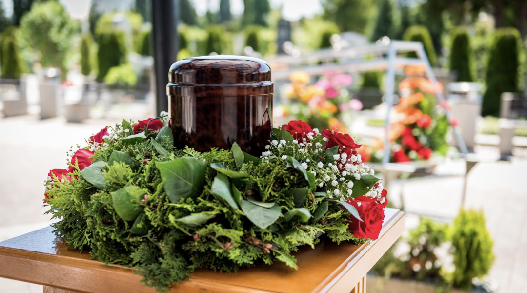 戶外墓園中擺放於木桌上的寵物骨灰罈,周圍以綠葉與紅玫瑰花圈環繞,氛圍莊重溫馨